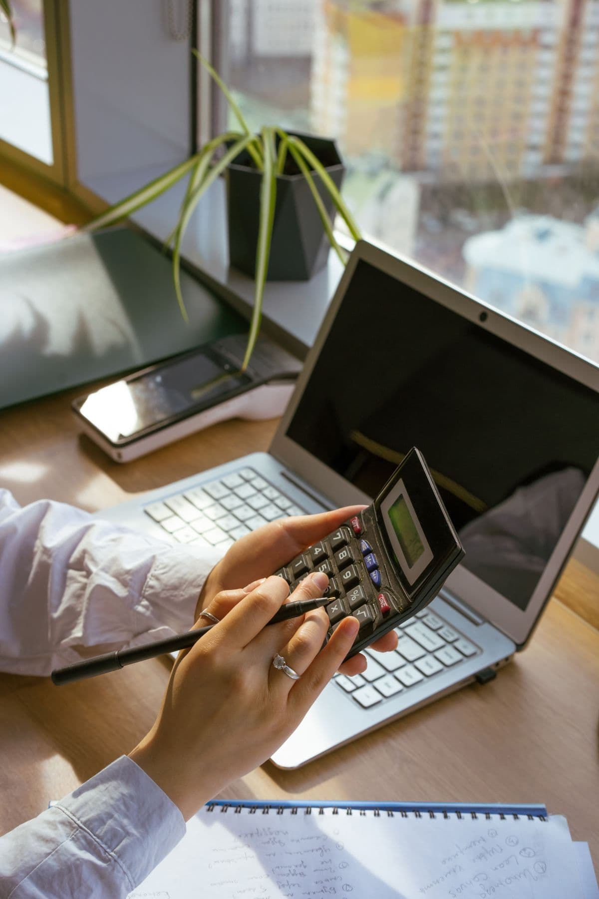 Mão usando uma calculadora sobre um notebook aberto, em um escritório